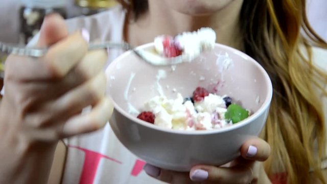 Girl eats Ricotta with fresh berries. Cottage cheese, curd cheese or tvorog with berries in bowl. Healthy breakfast ingredients. fresh fruit, berries mint, a jar of honey with a spoon for honey 