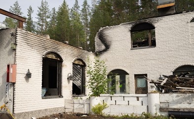 An old gas station building burned down. Collapsed roofing panes, darkened stinky walls, melted plastic details. Scandinavia, Europe.