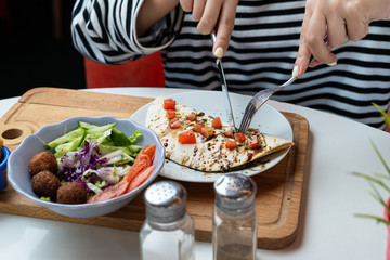 Young european woman is eating mexican quesadilla with knife and fork and cutting it in pieces