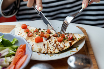 Young european woman is eating mexican quesadilla with knife and fork and cutting it in pieces
