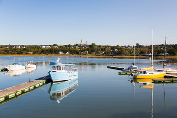 Obraz premium View of docked boats in small Trois-Pistoles marina, with 19th Century Notre-Dame-des-Neiges Church and other buildings in the background during a late summer afternoon, Quebec, Canada