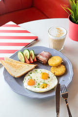 Traditional british breakfast with fried egg, wheat crunchy toasts, potato hash browns, bacon and salad