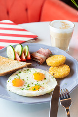 Traditional british breakfast with fried egg, wheat crunchy toasts, potato hash browns, bacon and salad