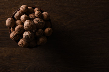  Walnuts nuts in a bowl on a dark brown wooden background in a dark key