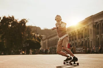 Foto op Canvas Portrait of handsome man in white shirt on sunset evening in summer. Stylish guy ride on skateboard on city street. Urban male lifestyle on buildings background © Yevhen
