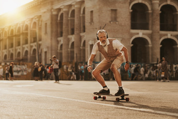 Fototapeta na wymiar Stylish handsome man ride on skateboard on city street in sunset evening. Smiling modern male portrait. Skater enjoy urban lifestyle