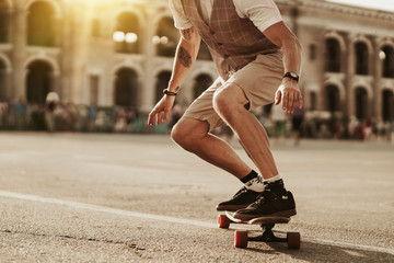 Urban man lifestyle. Stylish man ride on skateboard in white shirt on city street. Portrait of handsome bearded hipster male near road on buildings background. © Yevhen