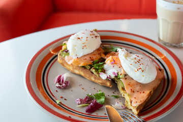 Fancy breakfast with soft waffle, mashed avocado, salmon, poached egg and coffee