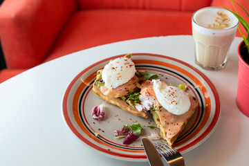 Fancy breakfast with soft waffle, mashed avocado, salmon, poached egg and coffee