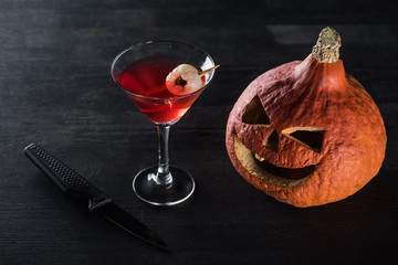 spooky Halloween pumpkin, knife and red cocktail on black background