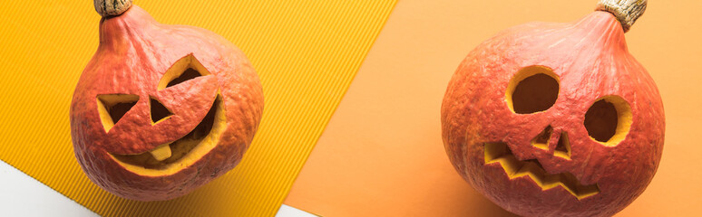 top view of carved spooky pumpkins on white and orange background, panoramic shot