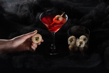 cropped view of woman holding decoration near red Halloween cocktail in black clouds