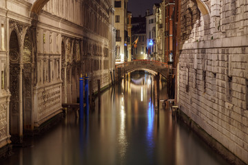 Naklejka premium Narrow canal between colorful historic houses in Venice at night.