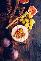 Camembert cheese with figs, walnuts, honey and thyme served for a dinner in dark key on  wooden background in retro style.  Toned image. Top view. Selective focus.