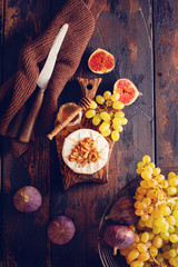 Camembert cheese with figs, walnuts, honey and thyme served for a dinner in dark key on  wooden background in retro style.  Toned image. Top view. Selective focus.