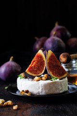 Camembert cheese with figs, walnuts, honey and thyme served for a dinner in dark key. Selective focus.