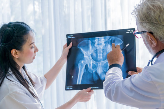 Senior doctor and young female nurse examining at the x-ray film of the human pelvis bones.  - Powered by Adobe