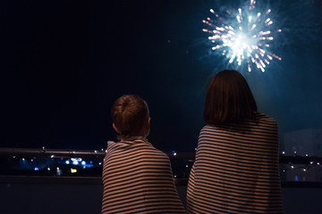 Mother and son looking at New Year celebration fireworks in night sky warmly wrapped in striped...