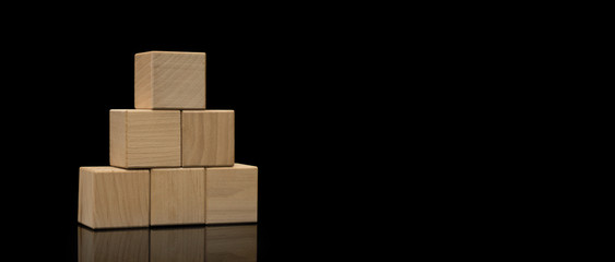 Wood cube arrange in pyramid shape on black background, business concept. Wooden blocks stacked in the shape of a pyramid.
