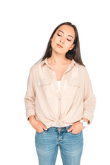 Obraz premium thoughtful asian woman holding hands in pockets while posing at camera isolated on white