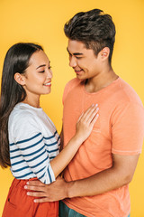 happy asian man and woman hugging while looking at each other isolated on yellow