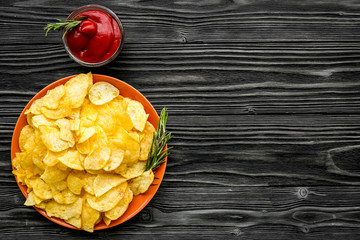 Junk food concept with heap of potato crisps and tomato sauce on wooden background top view space...