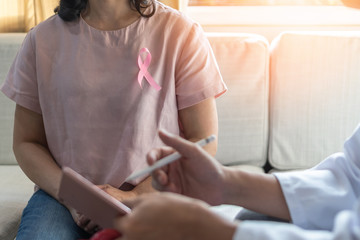 Breast cancer awareness with woman patient wearing pink ribbon consulting with doctor who...