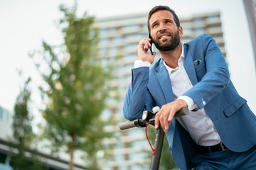 Young businessman talking on phone after riding electric scooter
