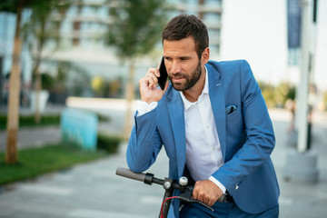 Young businessman talking on phone after riding electric scooter