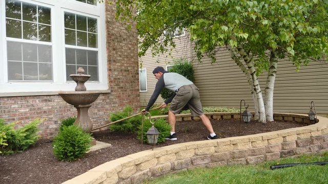 Man working in garden, raking, turning over mulch, landscaping in the spring summer, 60fps.