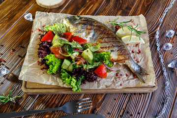 Grilled fish with vegetables and herbs on the kitchen board on a brown wooden background