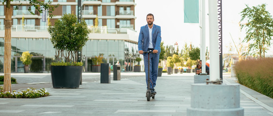 Young businessman in a suit riding an electric scooter © JustLife