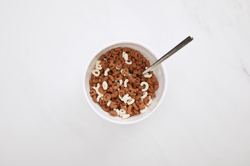 top view of bowl with chocolate and white cereal and spoon on marble surface