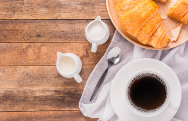 a cup of coffee with milk, sugar and croissant bread on wooden table, top view