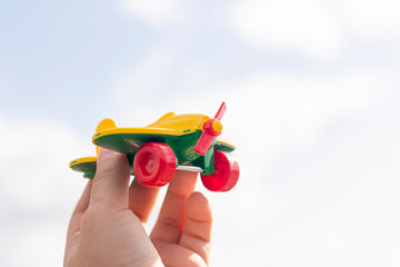 A small toy airplane in a man&rsquo;s hand against a blue sky with a blurred background. Travel concept