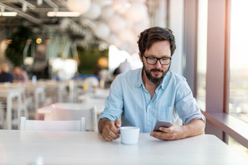 Fototapeta premium Young man using smartphone drinking coffee in a cafe 