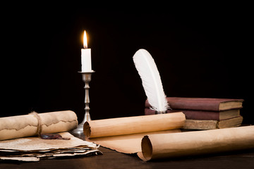 Scrolls of parchment and old papers and books on the background of a lit candle and inkwell pen