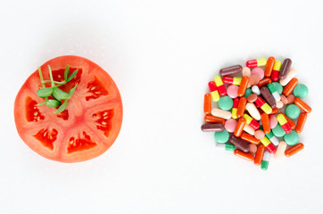 Fresh vegetables versus pills. A slice of tomato and fresh sprouts of sunflower against a heap of multi-colored pills on white background. Healthy eating concept. Copy space