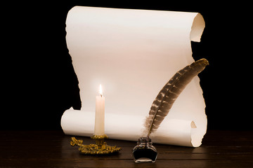A lit candle and quill with inkwell against a background of a scroll of parchment