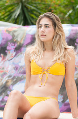 Blond haired model wearing a swimsuit at a pool.