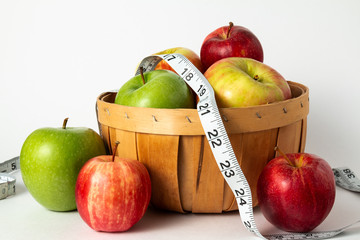 red and green apples in a basket with measuring tape and white background