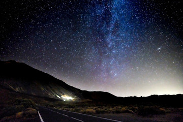 Concept of travel in amazing scenic places with long asphalt road by night and milky way stars on. the black sky