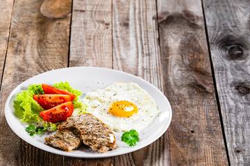 Grilled steaks with fried egg and vegetables on white plate