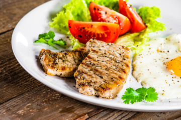 Grilled steaks with fried egg and vegetables on white plate