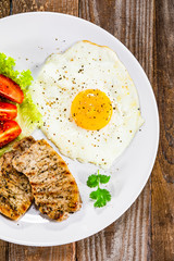 Grilled steaks with fried egg and vegetables on white plate