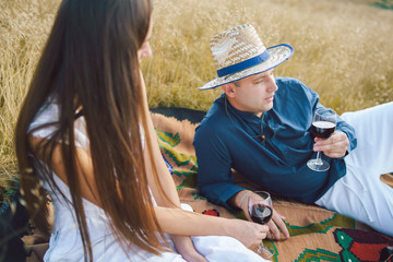 Young couple having a picnic on the blanket in the nature field on the mountain having a glasses of red wine celebrating love toasting on a date lovers happy in summer or autumn