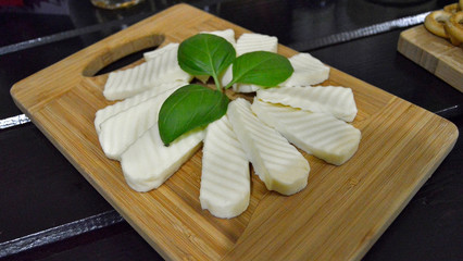 Fresh basil leaves and mozzarella slices on wooden cutting board