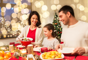 holidays, family and celebration concept - happy mother, father and little daughter having christmas dinner at home