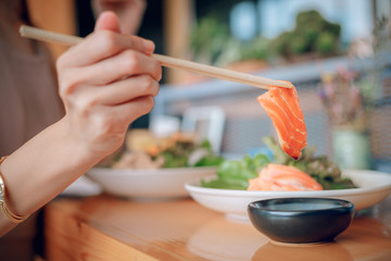 The hand is using a chopsticks to squeeze the salmon.