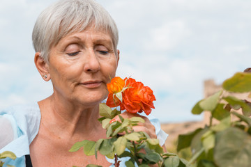 older woman with White hair smelling a rose in the garden, 65 years